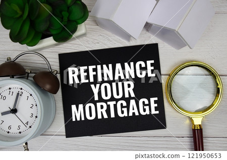 Refinance Your Mortgage text message with house model, alarm clock and magnifying glass top view on wooden background 121950653