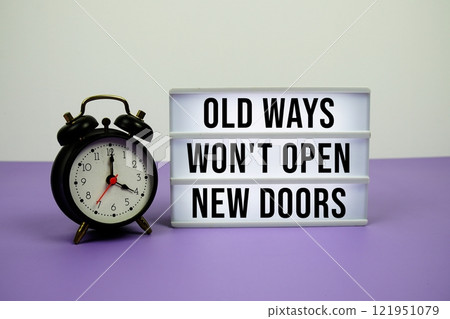 Old Ways Won't Open New Doors text on LED lightbox with alarm clock on purple background 121951079