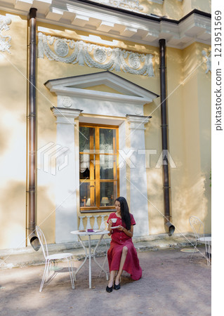 young African American woman in burgundy dress drinks tea in park in coffee shop 121951569