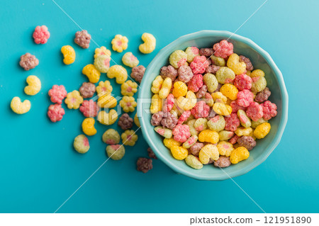 Colorful breakfast cereals in the shape of various fruit in bowl on blue background. Top view. Colorful breakfast cereals in the shape of various fruit in bowl on blue background. Top view. 121951890