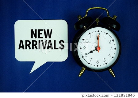 New Arrivals text on speech bubble with alarm clock top view on blue background 121951940