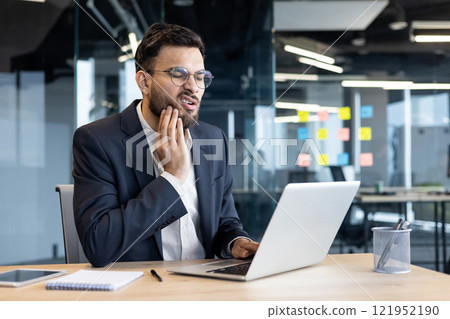 Toothache, sick man sitting at workplace, businessman holding jaw with hand, inflammation and pain in gums at workplace inside office. 121952190