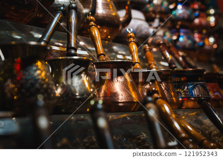 Copper and metal cezves with intricate engravings and wooden handles are arranged on a market shelf, reflecting Istanbul's cultural heritage. 121952343