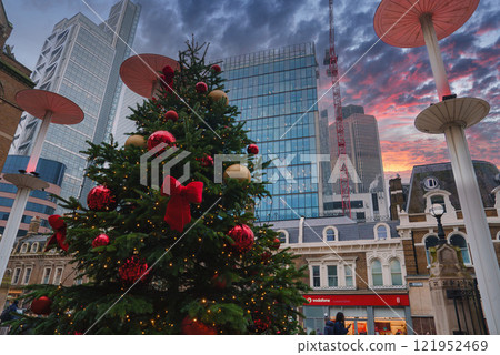 A large Christmas tree with red and gold ornaments stands in front of modern skyscrapers, including the Leadenhall Building, during a London sunset. A large Christmas tree with red and gold ornaments stands in front of modern skyscrapers, including the Leadenhall Building, during a London sunset. 121952469