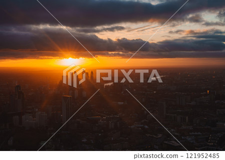 The image shows a sunset over London, highlighting skyscrapers and the River Thames. The sky is vibrant with dramatic clouds, reflecting the setting sun. The image shows a sunset over London, highlighting skyscrapers and the River Thames. The sky is vibrant with dramatic clouds, reflecting the setting sun. 121952485