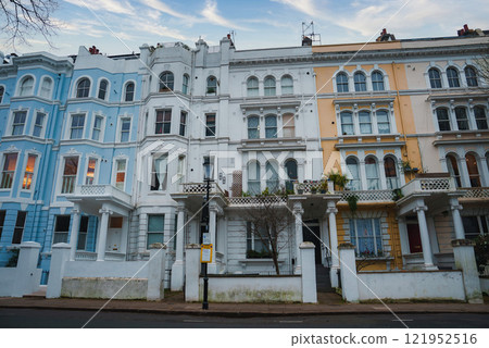 A row of colorful Victorian terraced houses in London features ornate details, pastel hues, large bay windows, and decorative balconies under a clear winter sky. 121952516