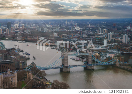 The image captures an aerial view of London's Tower Bridge over the River Thames, with a mix of modern and historic architecture under soft, diffused light. The image captures an aerial view of London's Tower Bridge over the River Thames, with a mix of modern and historic architecture under soft, diffused light. 121952581