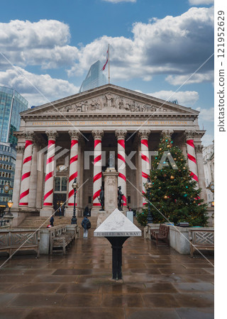 The Royal Exchange in London features festive red and white decorations. A large Christmas tree stands by the entrance, with a modern skyscraper in the background. The Royal Exchange in London features festive red and white decorations. A large Christmas tree stands by the entrance, with a modern skyscraper in the background. 121952629