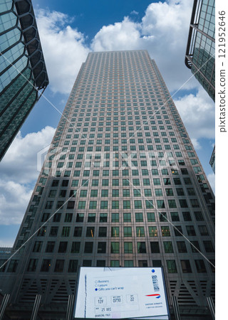 View of One Canada Square with its pyramid roof, flanked by modern glass buildings under a partly cloudy sky in London's financial district. 121952646