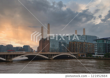 Battersea Power Station's four chimneys stand tall against a warm sunset sky. A bridge crosses the River Thames, blending historic and modern architecture. 121952664
