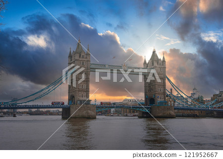 Tower Bridge in London is silhouetted against a vibrant sunset sky. Gothic style towers and suspension elements are visible, with buses crossing above. Tower Bridge in London is silhouetted against a vibrant sunset sky. Gothic style towers and suspension elements are visible, with buses crossing above. 121952667