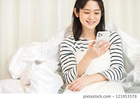 Young woman looking at a smartphone in the bedroom Young woman looking at a smartphone in the bedroom 121953578