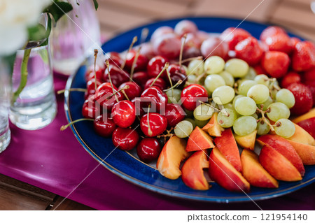 Fresh fruit platter with strawberries, grapes, and peaches on table, perfect for summer events Fresh fruit platter with strawberries, grapes, and peaches on table, perfect for summer events 121954140