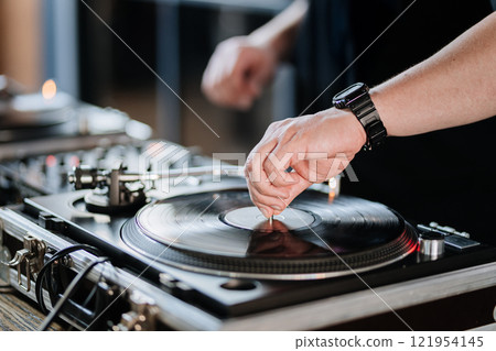 DJ mixing vinyl records on a turntable, creating an energetic vibe for a live music event DJ mixing vinyl records on a turntable, creating an energetic vibe for a live music event 121954145