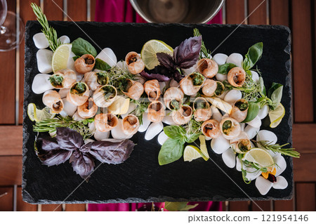 Gourmet escargot platter with fresh herbs and lemon, elegantly presented on a slate serving board Gourmet escargot platter with fresh herbs and lemon, elegantly presented on a slate serving board 121954146