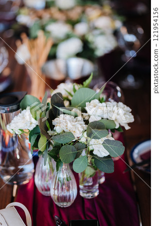 Elegant floral centerpiece with white roses and greenery on a table for a refined event setting Elegant floral centerpiece with white roses and greenery on a table for a refined event setting 121954156