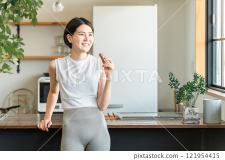 年輕的亞洲女性練瑜珈穿著吃蛋白質棒/營養棒 年輕的亞洲女性練瑜珈穿著吃蛋白質棒/營養棒 121954415