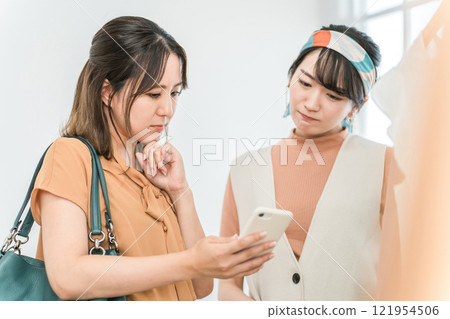 一位女顧客在服飾店購物時看著智慧型手機,憂心忡忡。 一位女顧客在服飾店購物時看著智慧型手機,憂心忡忡。 121954506