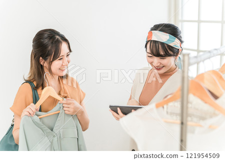 A female clerk and a customer checking inventory using a tablet at an apparel shop (inventory management, product management) 121954509