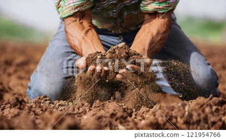 A farmer kneeling and holding soil, symbolizing the vital connection between humans and the land, the importance of sustainable agriculture, and the need for soil preservation and environmental A farmer kneeling and holding soil, symbolizing the vital connection between humans and the land, the importance of sustainable agriculture, and the need for soil preservation and environmental 121954766