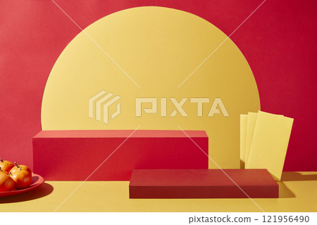 A minimalist product display setup with a backdrop of red and yellow for the Chinese New Year theme. Close-up of two empty red rectangular platforms, a plate of tangerines, and yellow envelopes. 121956490