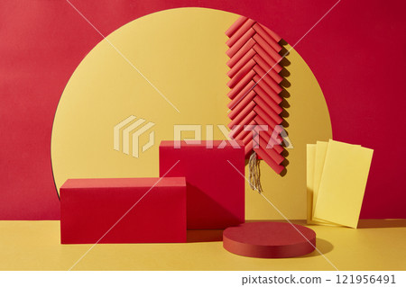 A Chinese New Year with a red and yellow background. Close-up of a round podium and two empty red rectangular platforms for presentation products, decorated by a firework string and yellow envelopes. 121956491