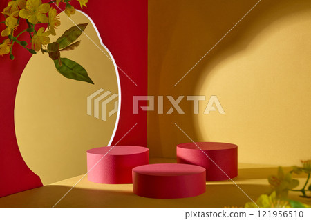 Perfect for the Chinese New Year, frontal perspective shows a red wall adorned with branches of yellow apricot blossoms. Some red cylindrical pedestal for product display against a yellow background, 121956510