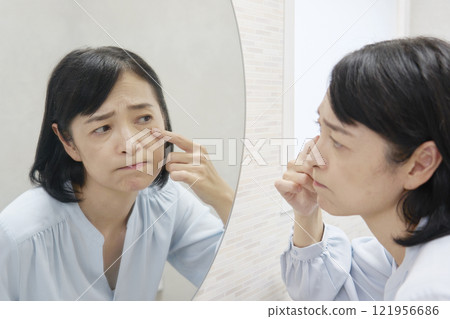 A woman in her 50s worries about dark circles under her eyes in the mirror A woman in her 50s worries about dark circles under her eyes in the mirror 121956686