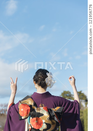 Image of a women's coming-of-age ceremony: A young woman in a kimono showing the number 20 with her hand, view from behind 121956776