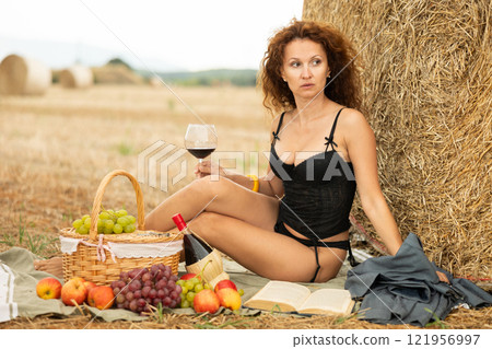 Sensual woman in black lingerie sitting by haystack during picnic alone Sensual woman in black lingerie sitting by haystack during picnic alone 121956997