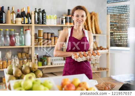 Female seller selling food products offers to buy chicken eggs in supermarket 121957037