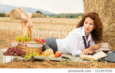 Businesswoman escaping to picnic with book and wine by hay bale 121957050