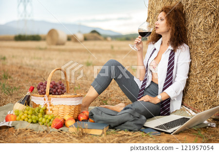 Woman in office clothes on picnic working on laptop and drinking wine while sitting near hay bales Woman in office clothes on picnic working on laptop and drinking wine while sitting near hay bales 121957054