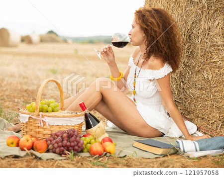 Woman sitting on ground in field, settled down in nature with book and glass of wine 121957058