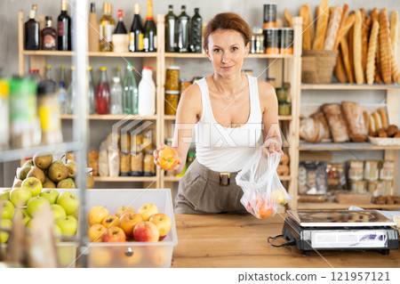 Adult woman seller weighs apples in bag 121957121