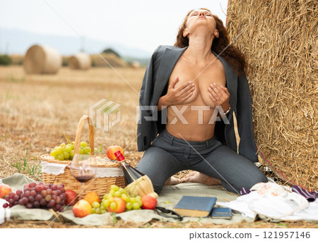 Topless girl in trousers is sitting with glass of wine and book near haystack 121957146