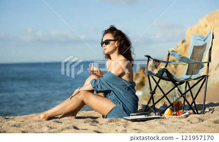 Relaxed woman savoring whiskey on sunlit ocean beach Relaxed woman savoring whiskey on sunlit ocean beach 121957170