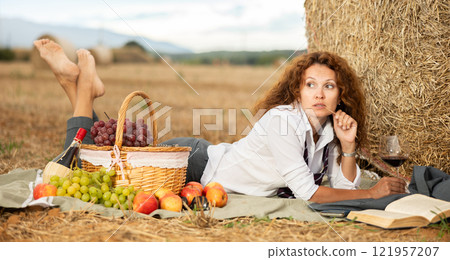 Relaxed businesswoman lying near haystack with wine and book Relaxed businesswoman lying near haystack with wine and book 121957207