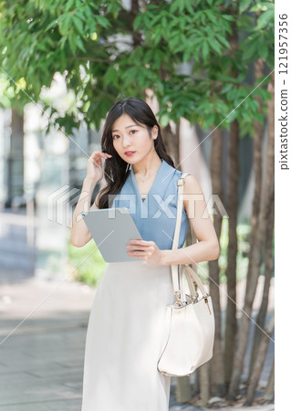 辦公區樹蔭下拿著平板電腦的女商人 辦公區樹蔭下拿著平板電腦的女商人 121957356