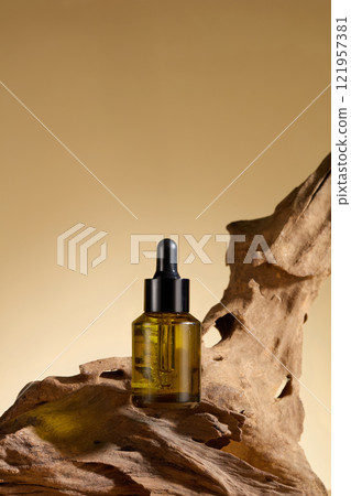 An advertisement for a beauty care product. Frontal view of a dark amber glass bottle containing a serum substance mockup, displayed on a piece of bleached driftwood against a beige backdrop. 121957381