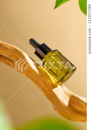 On the front of a piece of bleached driftwood with some green plants, a green amber glass bottle with a mockup of a serum is displayed against a beige background. A commercial for a beauty product. On the front of a piece of bleached driftwood with some green plants, a green amber glass bottle with a mockup of a serum is displayed against a beige background. A commercial for a beauty product. 121957394