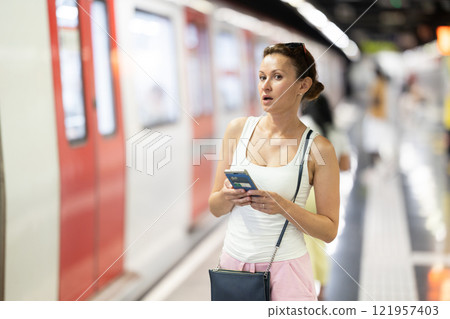 Portrait of gorgeous woman waiting for subway train with smartphone in hands at underground station 121957403