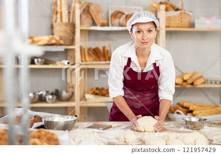 Cheerful woman baker kneading dough in bakery Cheerful woman baker kneading dough in bakery 121957429