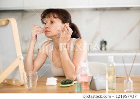 Woman checking facial skin condition in mirror at home Woman checking facial skin condition in mirror at home 121957437