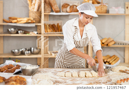 Skilled female baker slicing dough in artisan bakery 121957467