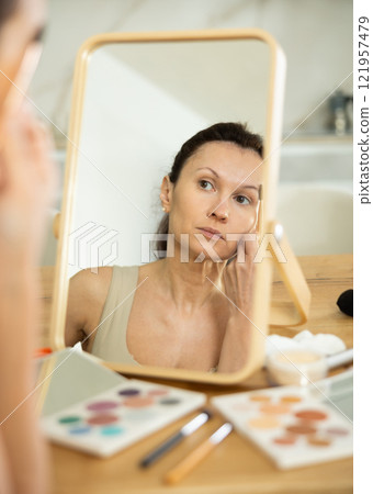 Middle-aged woman doing eyebrow make-up looking in the mirror Middle-aged woman doing eyebrow make-up looking in the mirror 121957479