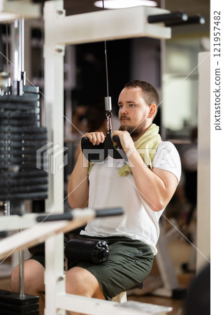 Man in gym performs exercises for arm muscles using cable crossover machine and pull weighted rope Man in gym performs exercises for arm muscles using cable crossover machine and pull weighted rope 121957482
