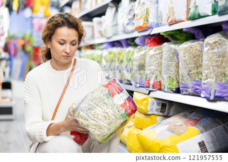 Interested woman choosing package with dry hay in pet store Interested woman choosing package with dry hay in pet store 121957555