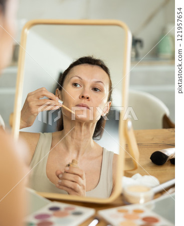 Middle-aged woman applying liquid foundation on her face Middle-aged woman applying liquid foundation on her face 121957654