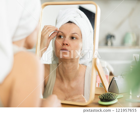 Middle-aged woman examining her facial skin looking in the mirror put on the table Middle-aged woman examining her facial skin looking in the mirror put on the table 121957655